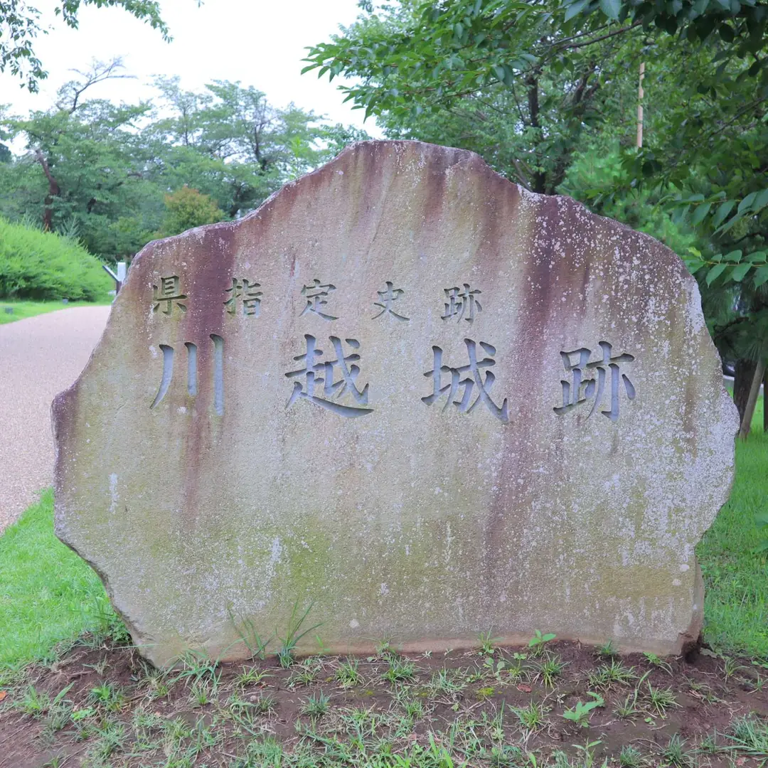 「県指定史跡 川越城跡」と刻まれた石碑。緑に囲まれた園路のそばに立つ。