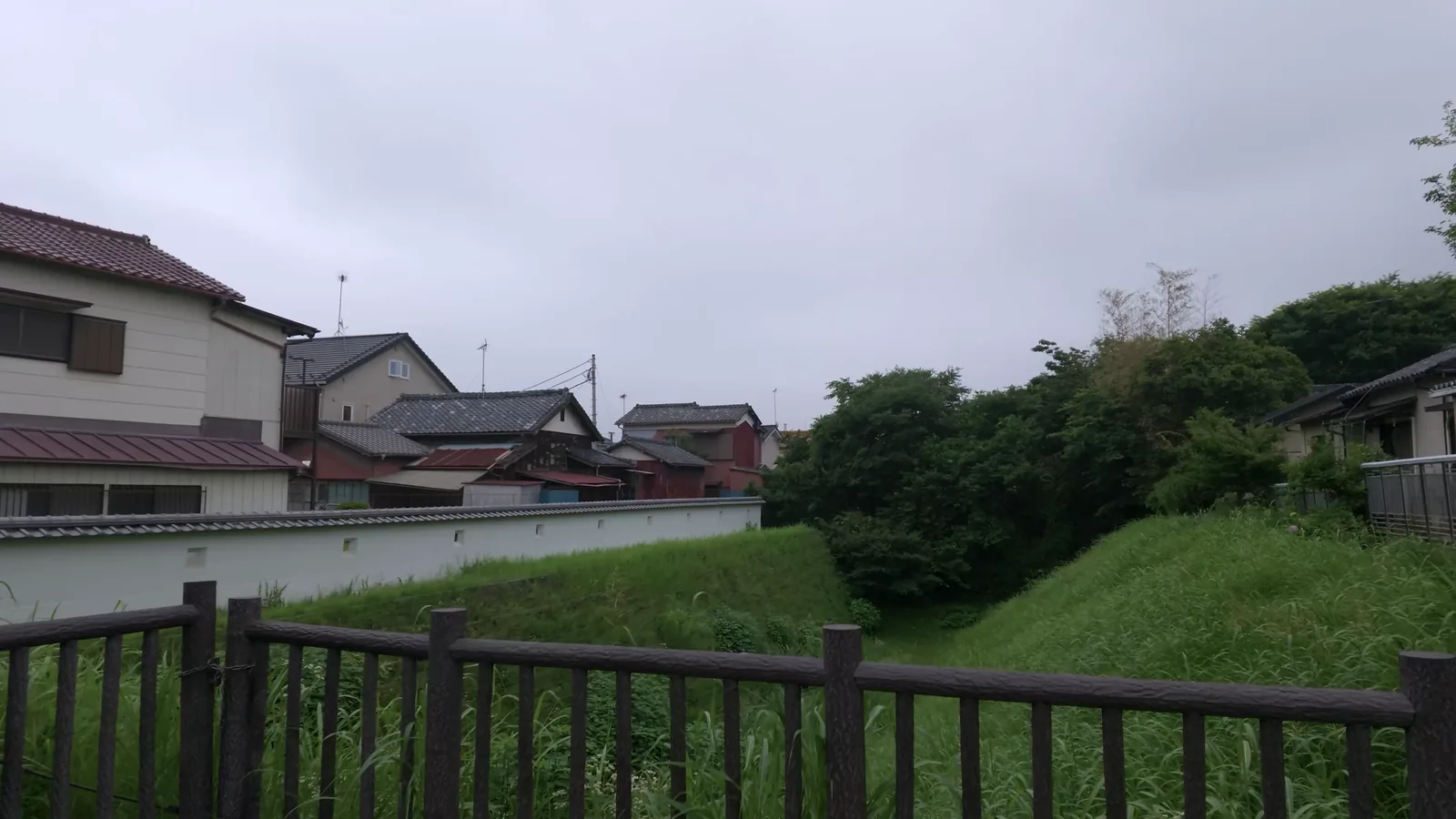 中ノ門堀跡。柵の向こうに草に覆われた大きなV字の窪みが続き、その先は住宅街になっている。