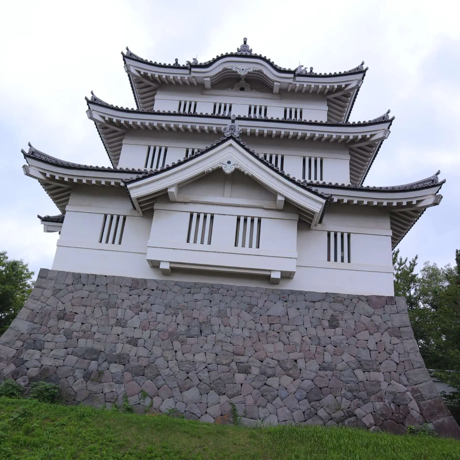忍城御三階櫓の正面。石垣の上に三層の白壁の櫓が立ち、手前は芝生。