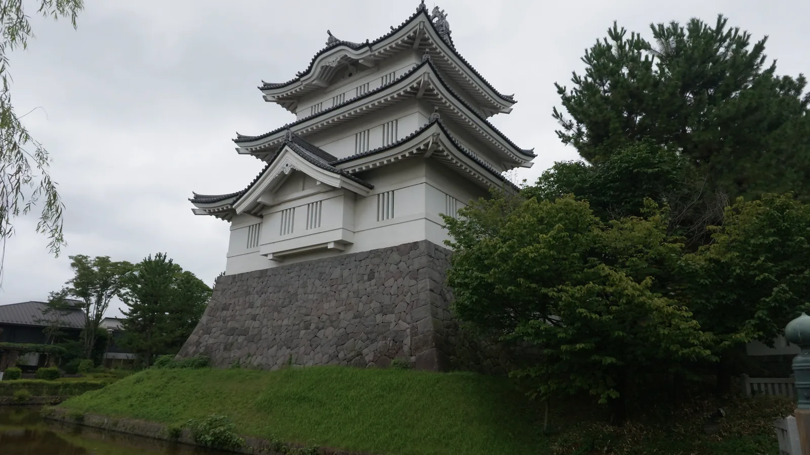 水堀の向こう、石垣の上に立つ忍城御三階櫓。白壁に黒い瓦屋根、空は一面の曇り。