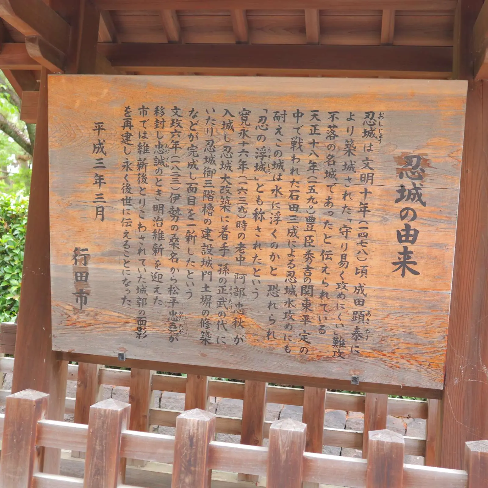 「忍城の由来」と題された木の案内板。平成三年三月 行田市と刻まれている。
